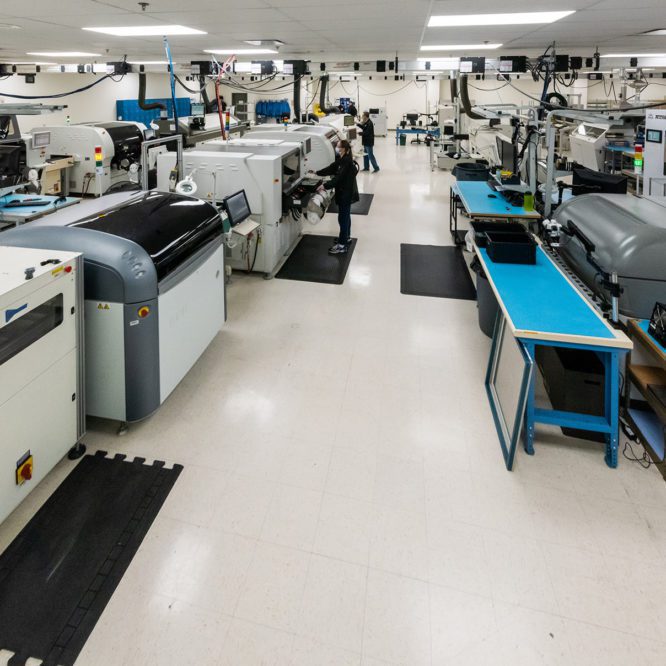 Wide view of a modern manufacturing facility with various high-tech machinery and a few workers monitoring production.