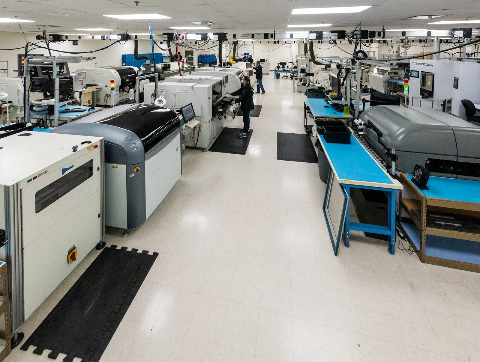 Wide view of a modern manufacturing facility with various high-tech machinery and a few workers monitoring production.