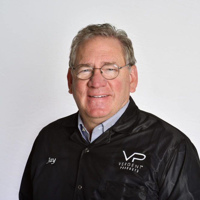 Portrait of a smiling man named Jay wearing glasses and a black jacket with "VP Vergent Products" logo.
