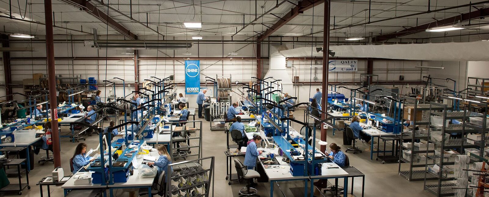 Electronics assembly facility with workers in blue coats handling components, illustrating what occurs in contract manufacturing.