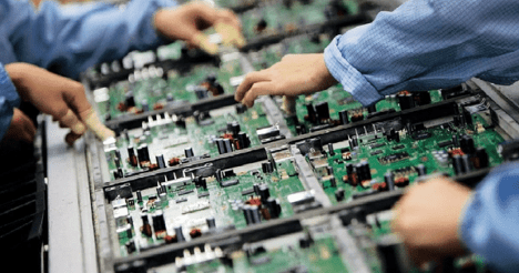 Technicians assembling green circuit boards on a production line in an electronics manufacturing facility.